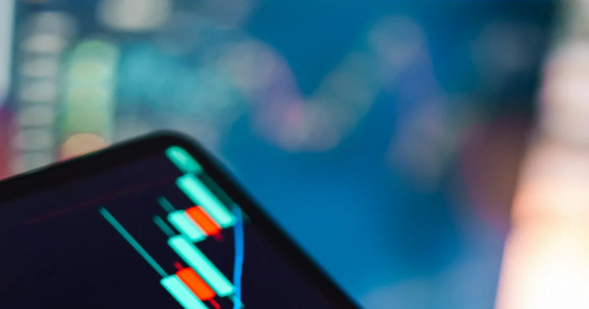 A hand holding a tablet showing a rising candlestick stock chart